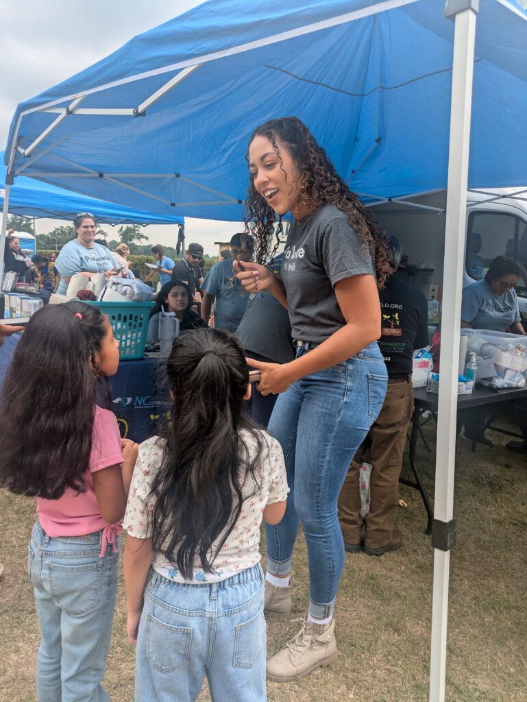 A young woman talks to two children at an event.